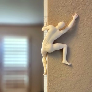 May include: A matte off-white wall-mounted sculpture of a human figure in a climbing pose, positioned on the corner of a wall. The figure is depicted reaching upward with one arm and bracing with a leg. The text kandies3d.etsy.com is visible.