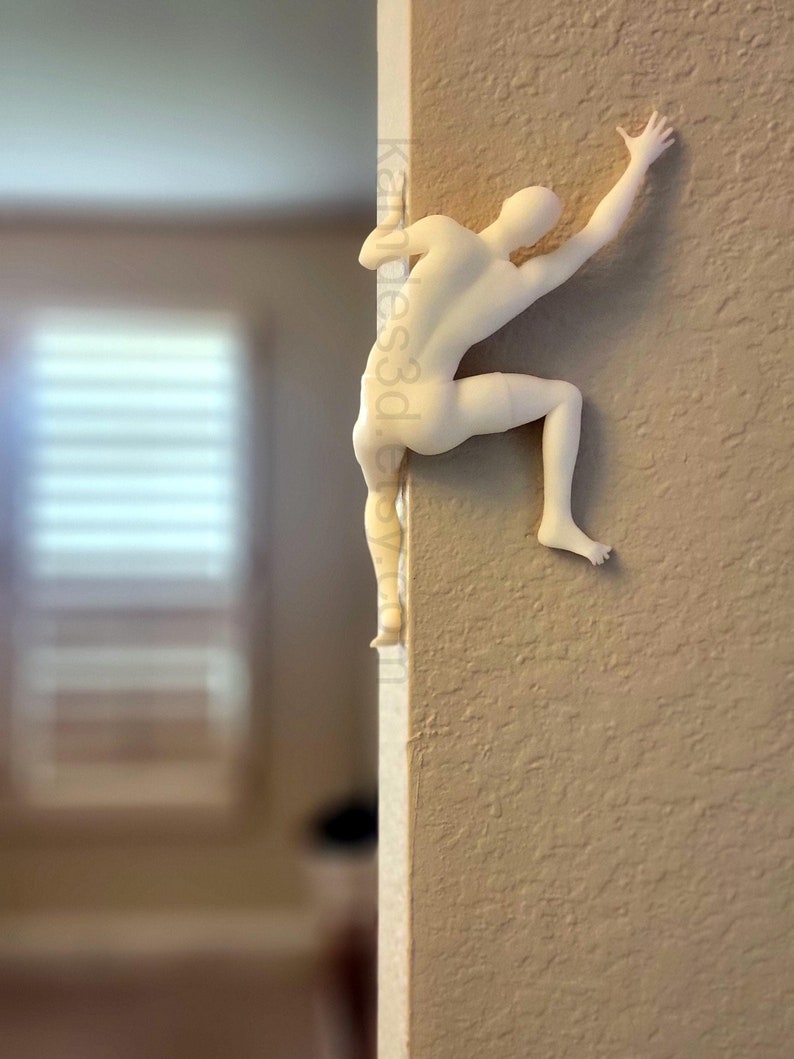 May include: A matte off-white wall-mounted sculpture of a human figure in a climbing pose, positioned on the corner of a wall. The figure is depicted reaching upward with one arm and bracing with a leg. The text kandies3d.etsy.com is visible.