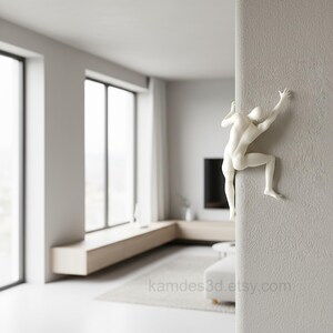 May include: A white wall-mounted sculpture depicting a human figure in a climbing pose, with arms and legs extended as if scaling the vertical edge of a textured wall. The figure is smooth, matte, and minimalist in its anatomical representation.