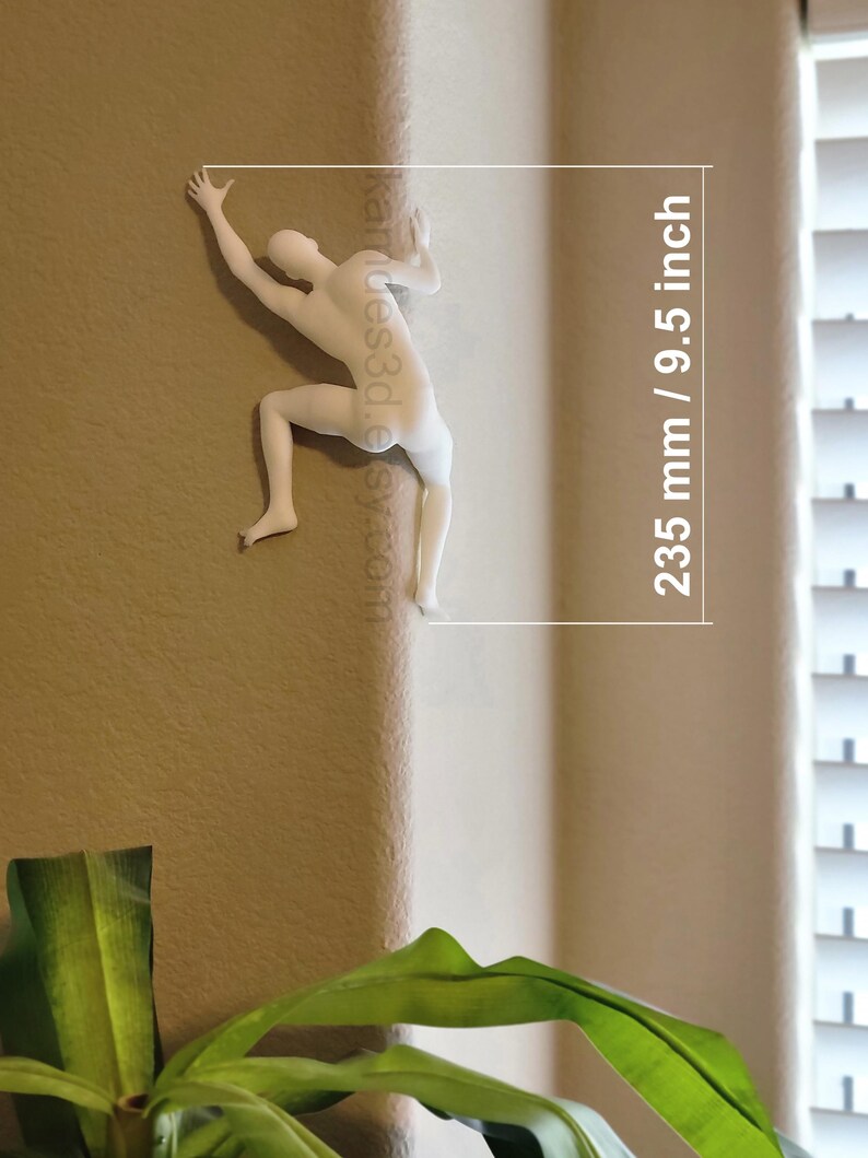May include: A white wall-mounted sculpture of a human figure climbing a corner. The figure is depicted in a dynamic pose with arms and legs extended. Text on the image indicates a height of 9.5 inches, which corresponds to 235 mm.