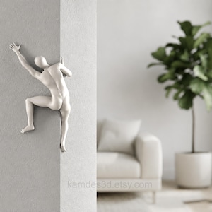 May include: A matte white wall sculpture depicting a stylized human figure climbing around the corner of a wall. The figure is shown in a dynamic pose with one arm extended upward and legs bent as if gripping the edge of the wall surface.