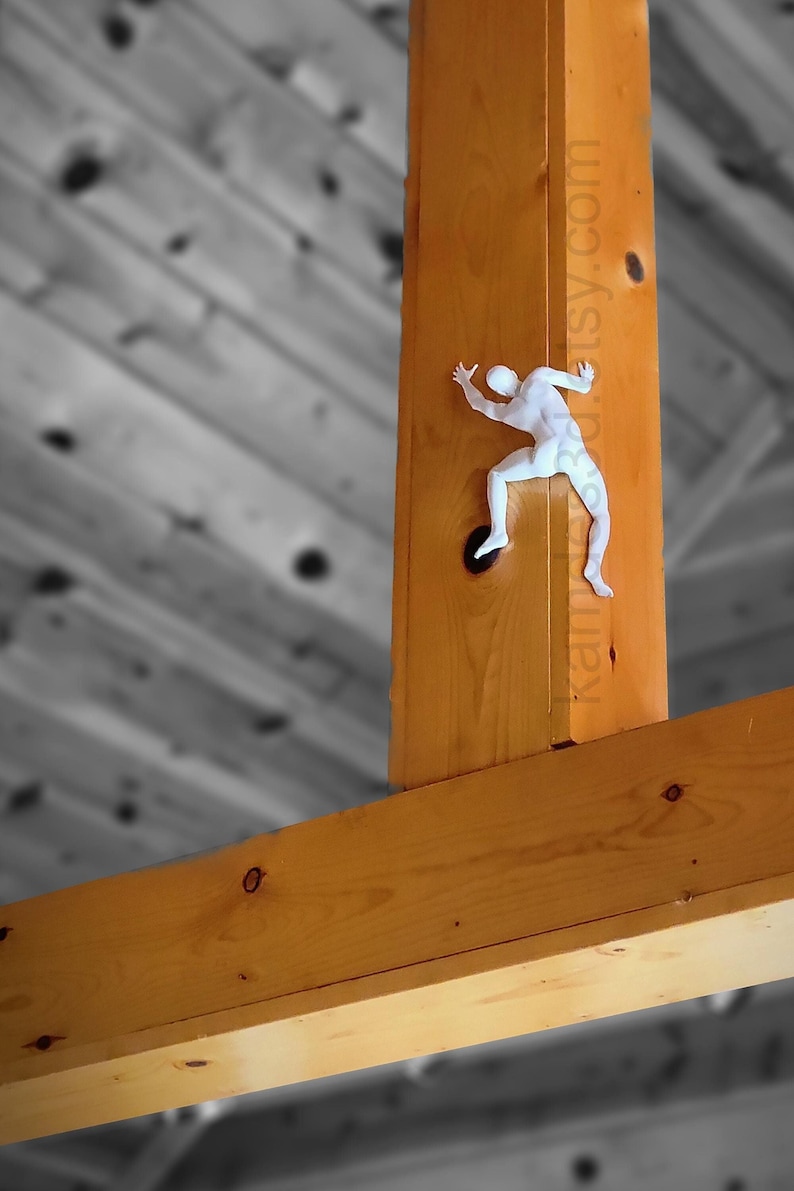May include: A white, three-dimensional figure of a person climbing, mounted on a vertical wooden beam. The figure is depicted in a dynamic pose with limbs extended as if scaling the wood. The text kamy3d.etsy.com is visible on the beam.