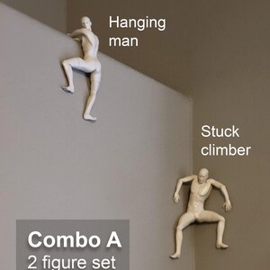 May include: A set of two off-white wall-mounted figurines. One figure is labeled 'Hanging man' and is positioned over a ledge. The second figure is labeled 'Stuck climber' and is positioned in a corner. The set is labeled 'Combo A 2 figure set as shown'.