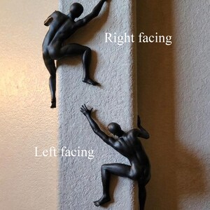 May include: Two matte black wall sculptures depicting human figures in a climbing pose. One figure is positioned as right facing, while the other is positioned as left facing. The figures are shown with arms and legs extended as if scaling a vertical surface.