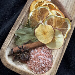 May include: A wooden tray filled with dried fruit, spices, and pink Himalayan salt. The fruit includes orange and apple slices. The spices include cinnamon sticks, star anise, and cloves.