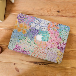 May include: A floral patterned laptop case featuring a colorful array of flowers in shades of pink, purple, blue, and orange. The case is designed to fit a laptop, with a cutout for the Apple logo. The case is on a wooden surface.