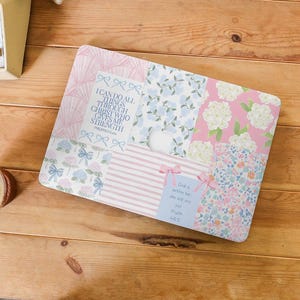 May include: A laptop skin with a patchwork design featuring floral patterns in shades of pink and blue. The skin includes inspirational quotes, including "I can do all things through Christ who gives me strength" and "God is with us, she will not fail".