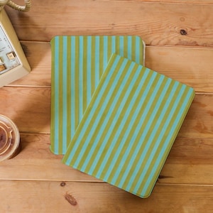 May include: Two rectangular placemats with vertical stripes in light blue and olive green. They are placed on a wooden surface. A vintage telephone and a coffee cup are visible in the background.