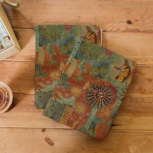 May include: Two notebooks with a colorful, patterned design featuring turtles playing instruments, suns, and figures. The notebooks have a vintage, artistic aesthetic with a mix of red, blue, and yellow hues. The notebooks are on a wooden surface.