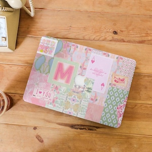 Puede incluir: Una funda decorativa para portátil con un diseño de patchwork en tonos pastel de rosa, verde y azul. El diseño incluye la letra "M", motivos de naipes, estampados florales y el texto "I ♥ YOU".