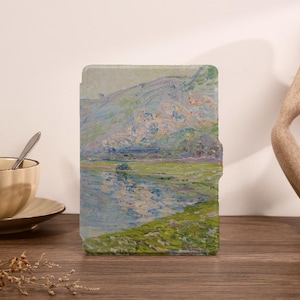 May include: A rectangular e-reader case featuring an impressionist-style landscape painting of a lake, rolling hills, and grassy banks in shades of blue, green, and soft pink. The case has a smooth, flat surface with a small side tab for opening.