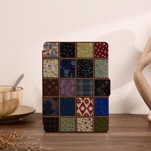 Op de afbeelding: Een rechthoekige tablethoes met een patchworkontwerp van twintig afzonderlijke vierkanten. Elk vierkant toont een uniek bloemen-, ruit- of geometrisch patroon in diverse kleuren zoals marineblauw, donkerrood, olijfgroen en crème, gescheiden door gouden stippen.