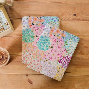 Peut inclure: Deux carnets à motifs floraux avec un design coloré composé de fleurs roses, bleues, jaunes et blanches. Les carnets sont empilés l'un sur l'autre sur une surface en bois.
