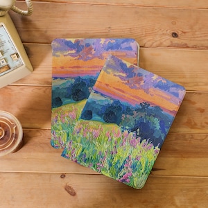 Könnte beinhalten: Zwei farbenfrohe Landschaftsbilder auf einer Holzoberfläche. Die Bilder zeigen einen Sonnenuntergang über einem Feld mit Wildblumen mit blauem Himmel und orangefarbenen und violetten Wolken.