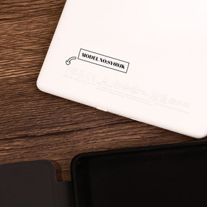 May include: A white electronic tablet device with rounded corners, featuring a black rectangular label printed with the text MODEL NO:SY69JK and a small arrow icon pointing toward the text, alongside various faint regulatory markings and symbols.