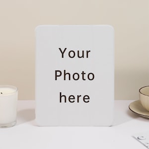 Puede incluir: Marco de fotos blanco con el texto "Your Photo here" impreso en él. El marco está sobre una superficie blanca.