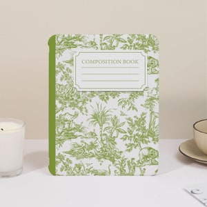 Könnte beinhalten: Ein grünes Schreibheft mit weißem Hintergrund und grünem Rand. Der Einband zeigt ein sich wiederholendes Muster aus schwarz-weißen Illustrationen von Bäumen, Vögeln und Tieren. Der Titel "COMPOSITION BOOK" ist in Schwarz auf einem weißen Etikett gedruckt.