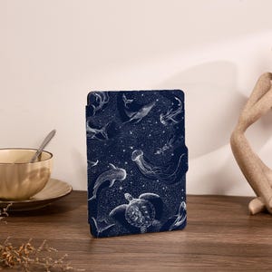 May include: A rectangular e-reader case in deep navy blue featuring a white line-art pattern of various marine life, including a sea turtle, a jellyfish, a whale, and sharks, set against a background of scattered white stars and celestial dots.