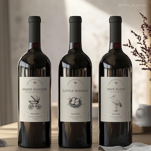 Puede incluir: Tres botellas de vino con etiquetas que dicen "Gran Reserva", "Pequeño Milagro" y "Bebé Felicidad". Cada etiqueta tiene una ilustración diferente: un cochecito de bebé, un nido con huevos y una cigüeña.