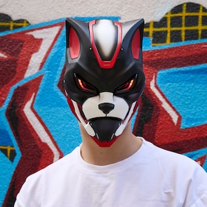 May include: A person wearing a black, red and white mask with glowing red eyes. The mask has a stylised animal face with pointed ears and a small, black nose.