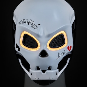 May include: White skull mask with black details and orange LED lights around the eyes. The mask has the words "Cry Baby" and "Alone" written on it, along with a red heart with a lightning bolt through it.
