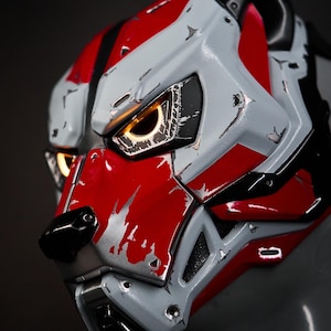 May include: A red and white helmet with a dog-like face. The helmet has a distressed paint finish and glowing yellow eyes.