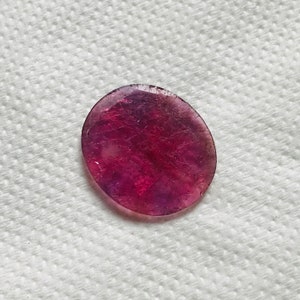Puede incluir: Una piedra preciosa redonda, facetada, p&uacute;rpura y rosa con una superficie lisa y pulida.