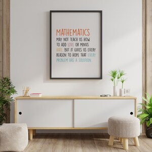 May include: A framed print with the text "MATHEMATICS" in orange, followed by a quote about love, hate, and solutions. The print hangs above a white cabinet with wooden accents, a small stool, and potted plants.