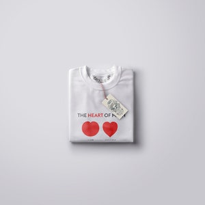 May include: White t-shirt with red hearts and the text "THE HEART OF MY" printed on the front. A brown tag with text is attached to the shirt.