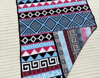May include: A black, blue, pink, and white crocheted throw blanket with geometric patterns. The blanket is folded in half and has a fringe on the edges.