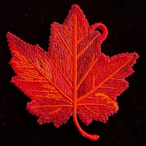 May include: A red embroidered maple leaf with a loop at the top. The leaf is detailed with stitching that creates a textured look.