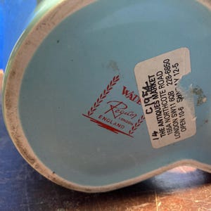 May include: A light blue ceramic pitcher with a white rim. The bottom of the pitcher features a red and white logo that says "Regal Wade England". A sticker with text is also visible.
