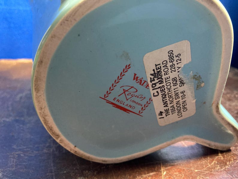 May include: A light blue ceramic pitcher with a white rim. The bottom of the pitcher features a red and white logo that says "Regal Wade England". A sticker with text is also visible.