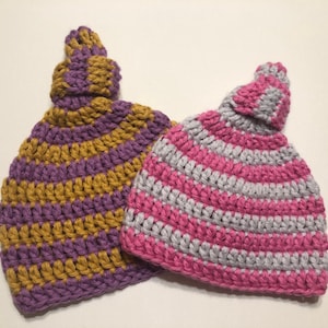 May include: Two crocheted hats with striped patterns. One hat is purple and gold, the other is pink and gray.