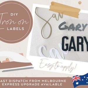 May include: DIY iron-on labels featuring the name "GARY" in black and grey lettering on a white fabric background. The image also includes an iron and a gold star sticker.