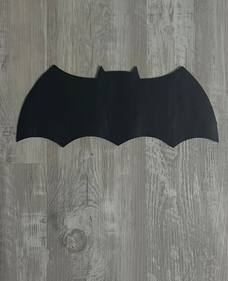 May include: A black felt bat silhouette cutout. The bat is on a light gray wood background.