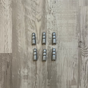 Può includere: Sette cappucci in metallo color argento per gambe di mobili. I cappucci sono disposti in due file di tre e una fila di uno.