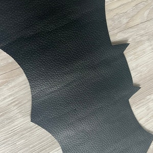 May include: Black leather bat wing shape cut out. The leather has a textured surface.