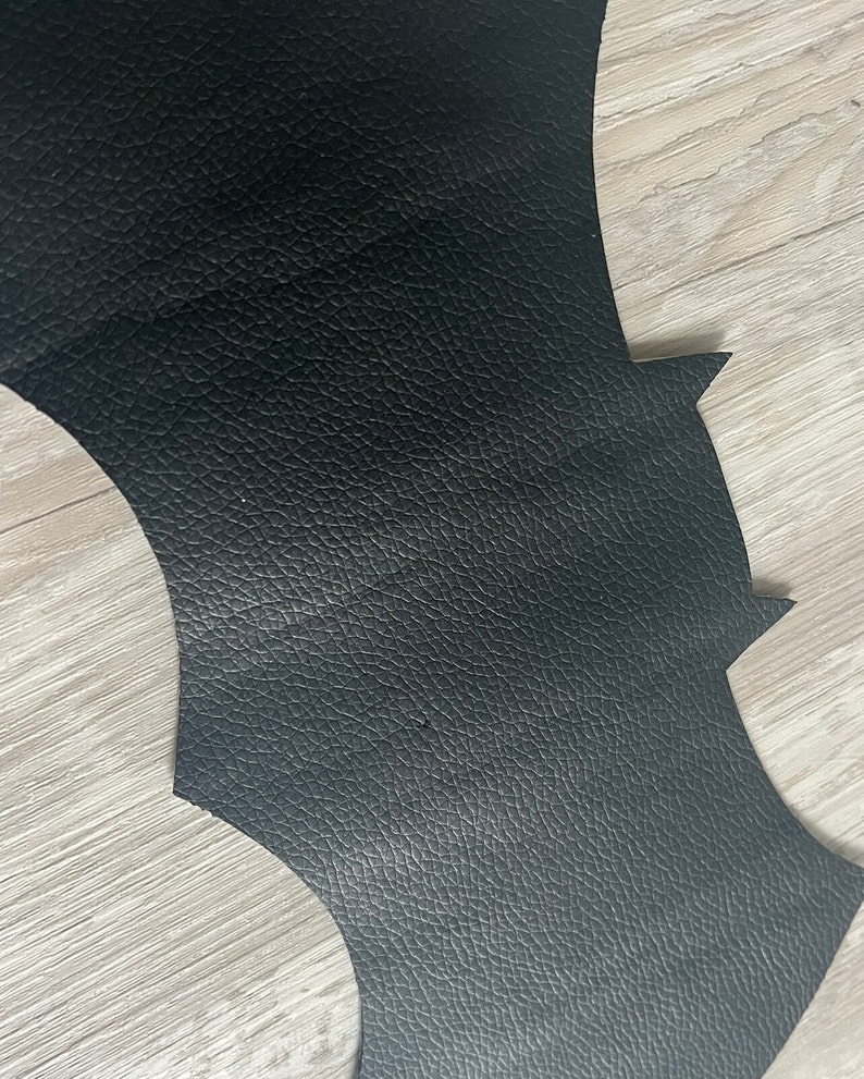 May include: Black leather bat wing shape cut out. The leather has a textured surface.