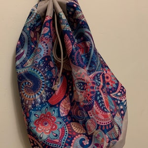 May include: A blue and pink paisley patterned drawstring bag with a gray bottom. The bag is hanging from a hook.