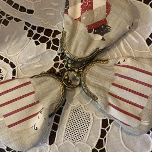 May include: Three small fabric coin purses with a chain connecting them. The purses are made of a beige fabric with red and white stripes and a black and white checked pattern. The purses have a gold metal frame.