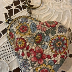 May include: A heart-shaped coin purse with a floral pattern in shades of red, yellow, blue, and green. The purse has a metal clasp and a key ring.