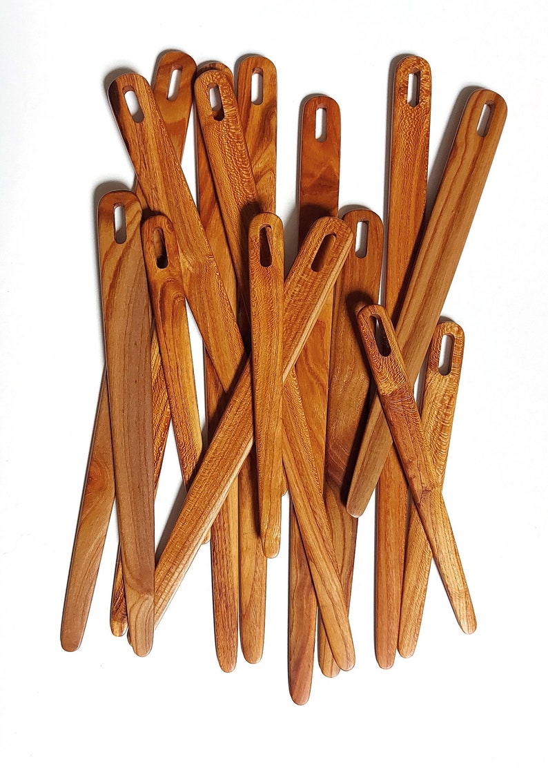 May include: A group of 14 wooden knitting needles with a natural brown finish. The needles are arranged in a random pattern, with some overlapping.