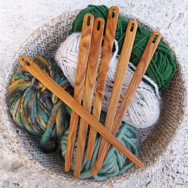 May include: Six wooden knitting needles with green yarn in a wicker basket. The needles are made of natural wood and have a smooth finish.