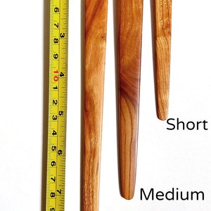 May include: Three wooden knitting needles of different lengths: short, medium, and long. The needles are made of light brown wood with a natural grain pattern. The needles have a loop at the top for holding yarn.