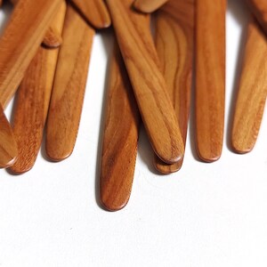 May include: A close-up of a pile of wooden butter knives. The knives are all made of light brown wood and have a smooth, rounded finish.