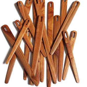 May include: A collection of wooden knitting needles, all in various shades of brown, are stacked on top of each other. The needles are all the same size and shape, and they have a smooth, polished finish.