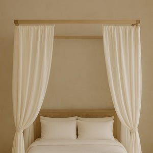 May include: A white bed with a wooden frame and white linen bedding. The bed has sheer white curtains hanging from the wooden canopy.