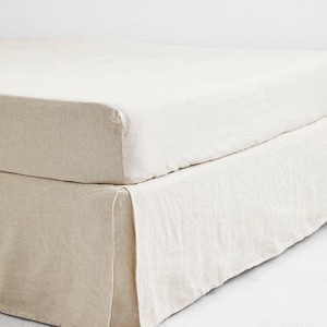 Może przedstawiać: Beżowy zestaw pościeli składający się z prześcieradła z gumką i spódnicy do łóżka. Tkanina ma teksturowany wygląd, a spódnica do łóżka ma plisowany design. Neutralna paleta kolorów sugeruje minimalistyczną lub naturalną estetykę, odpowiednią do dekoracji sypialni.