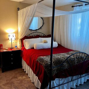 May include: A red canopy bed with a white canopy and a leopard print throw blanket. The bed has a white ruffled bed skirt and a white pillow with a stuffed animal on top.